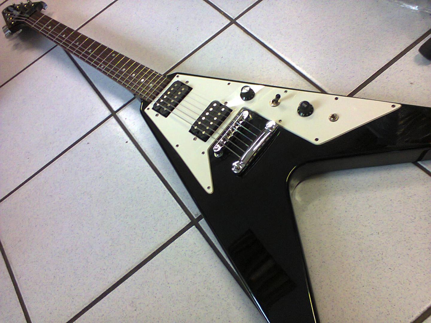 EPIPHONE FLYING V EBONY EPIPHONE FLYING V EBONY GUITARE ELECTRIQUE NOIRE VERNIE. CORPS AULNE. MANCHE ACAJOU. TOUCHE PALISSANDRE. 2 MICROS DOUBLE. VOL. TON. SELECTEUR 3 POS. MECANIQUE BAIN D'HUILE. PLAQUE BLANCHE ACCASTILLAGE CHROME.